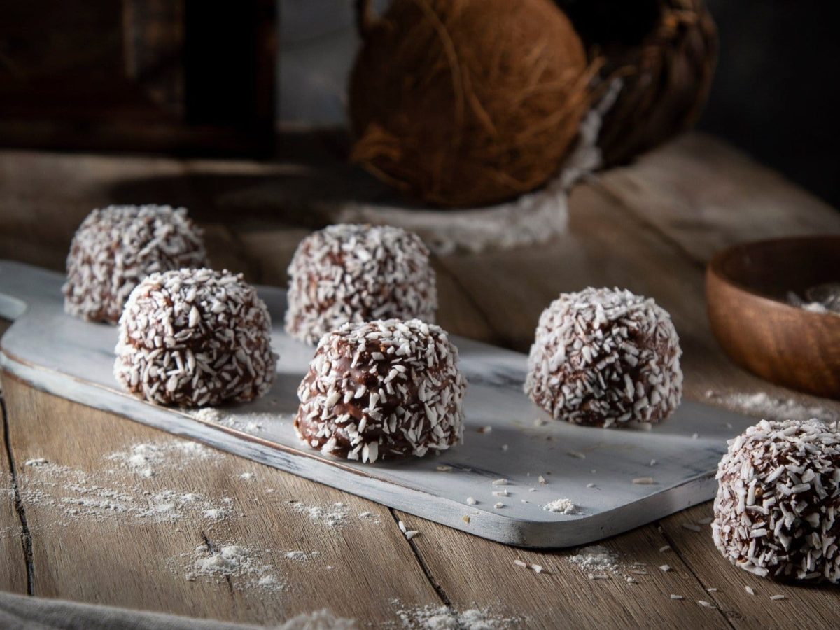 Dunkler Hintergrund: Auf einem rustikalen Holztisch liegen selbst gemachte selbst gemachte Weihnachts-Trüffel. die mit Kokosflocken bestreut sind.