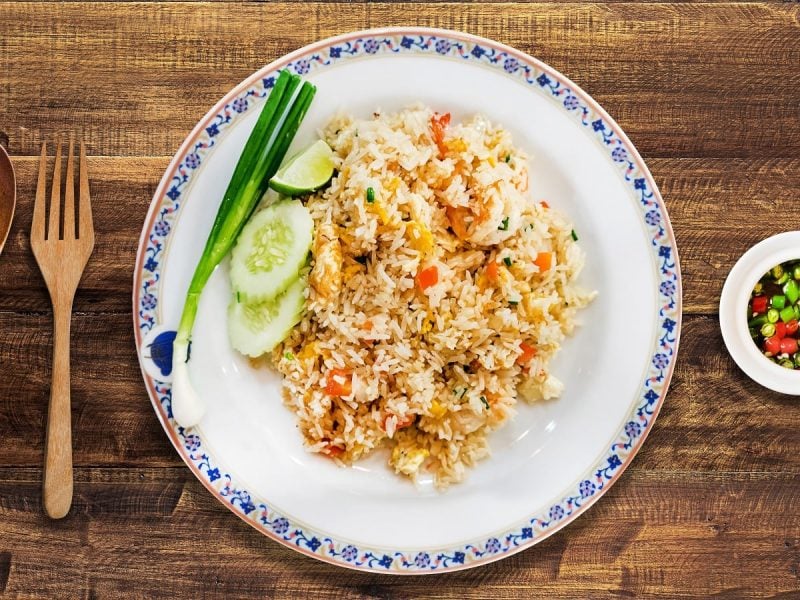 Ein weißer Teller mit Khao Pad auf einem Holztisch.