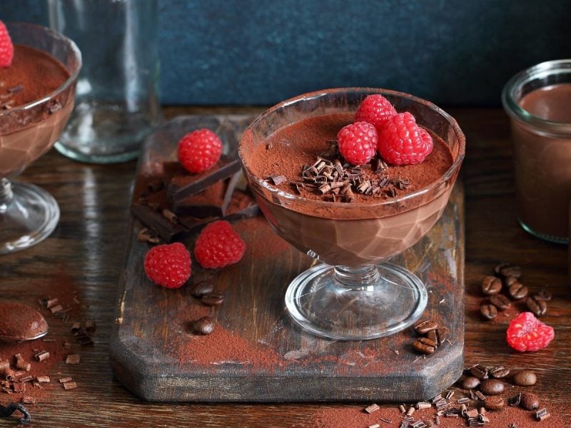 Ein Glas Schoko-Himbeer-Pudding auf einem Holzbrett.