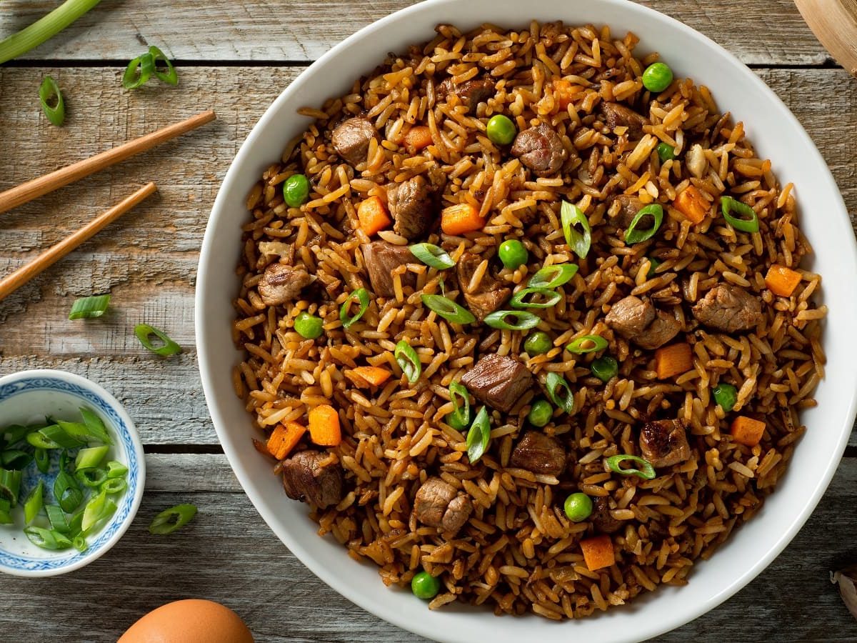 Ein Teller mit Beef Fried Rice auf einem Holztisch.