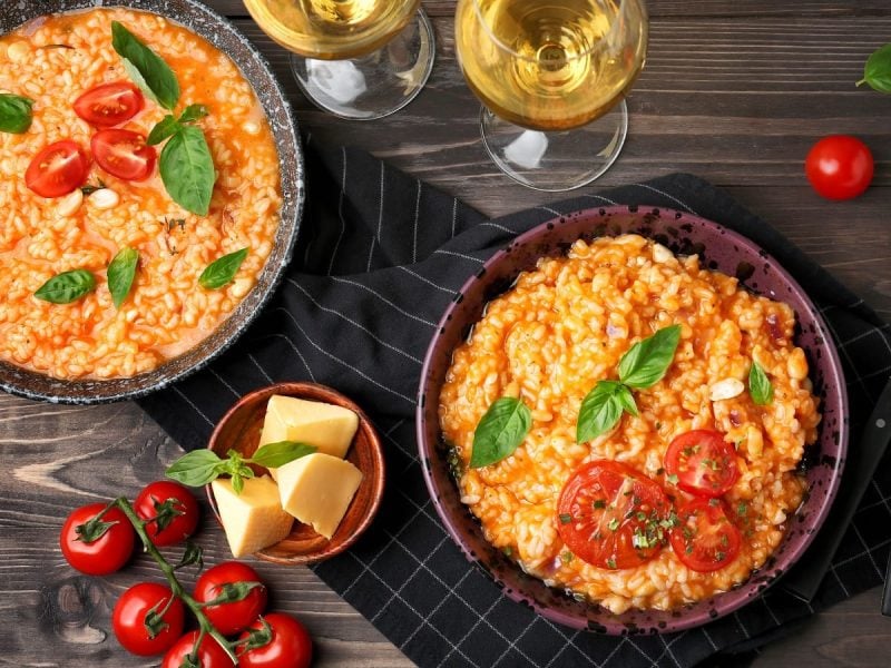 Zwei Teller mit Risotto alla pizzaiola auf einem Holztisch.