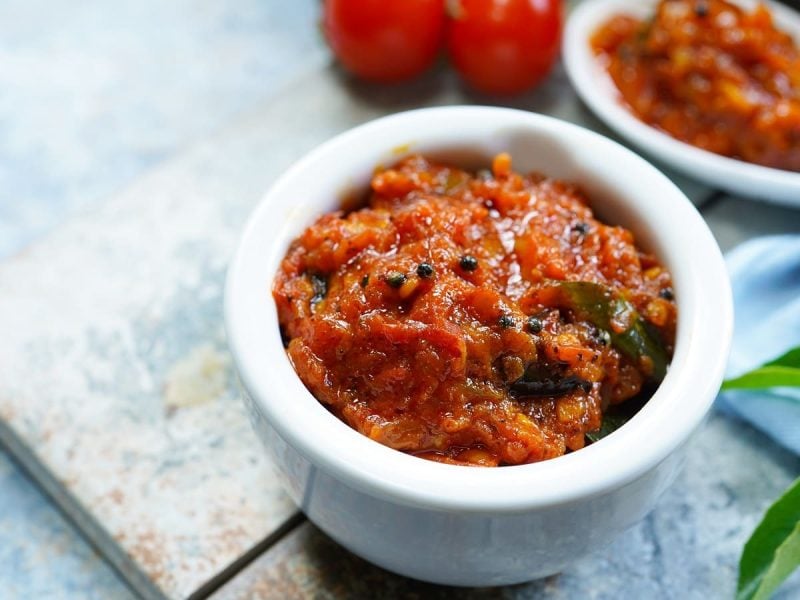 Eine kleine weiße Schüssel mit Tomaten-Chutney auf einem Marmorbrett.