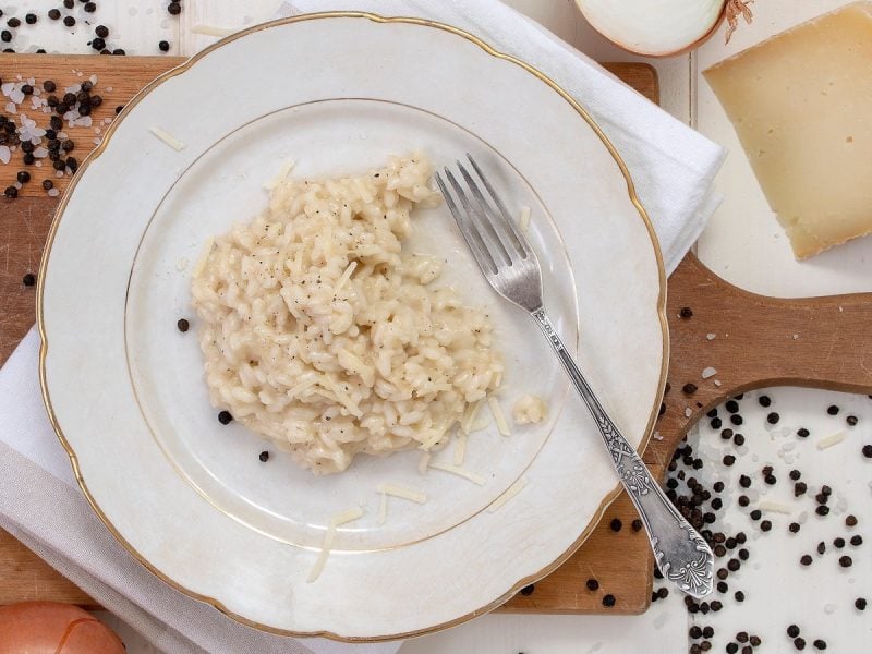 Ein weißer Teller mit Risotto Cacio e Pepe auf einem Holzbrett.