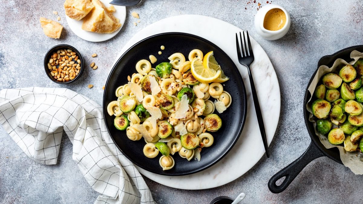 Ein Teller Rosenkohl-Pasta mit Zitronen-Buttersauce auf einem hellgrauen Untergrund.