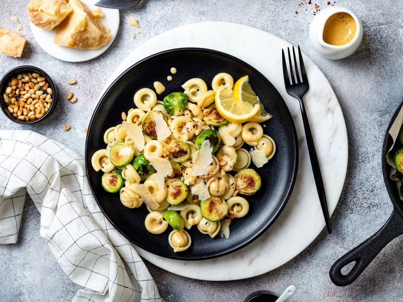 Ein Teller Rosenkohl-Pasta mit Zitronen-Buttersauce auf einem hellgrauen Untergrund.