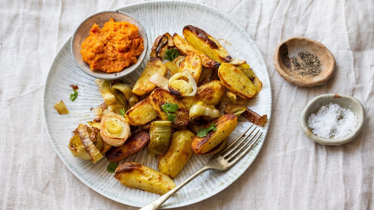 Ein Teller mit einer Portion Curry-Kartoffel-Pfanne auf einem hellen Holztisch.