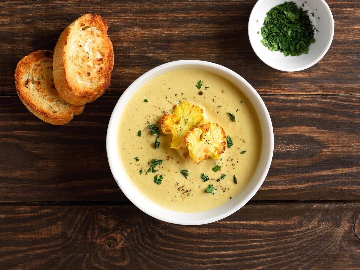 Eine Schüssel Curry-Blumenkohlsuppe auf einem dunklen Holztisch.