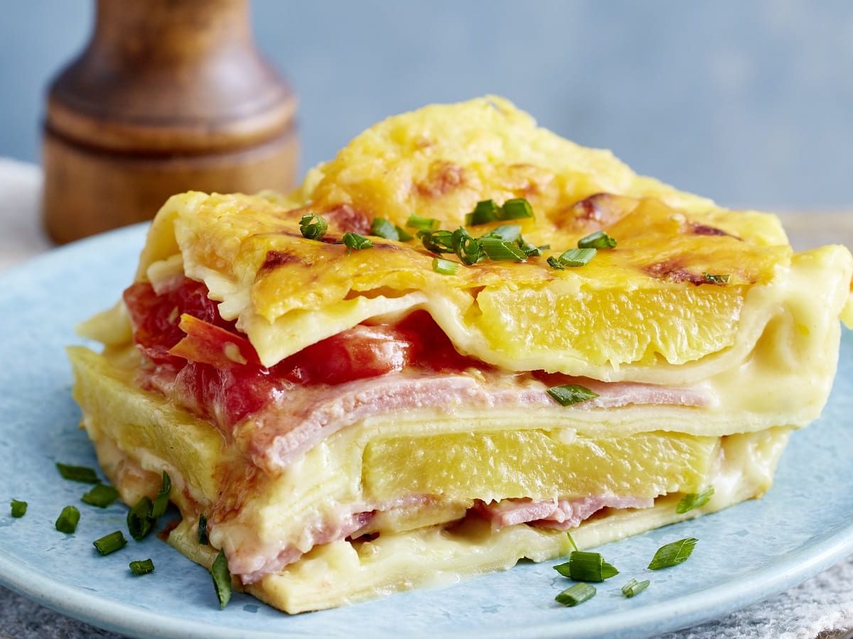 Ein hellblauer Teller mit einem Stück Lasagne Hawaii darauf.