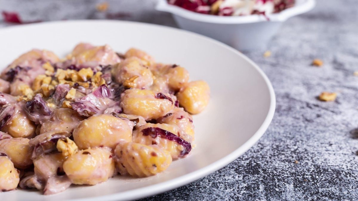 Draufsicht schräg: Ein Teller Gnocchi mit Radicchio in einer Walnuss-Sauce auf grauem Untergrund.