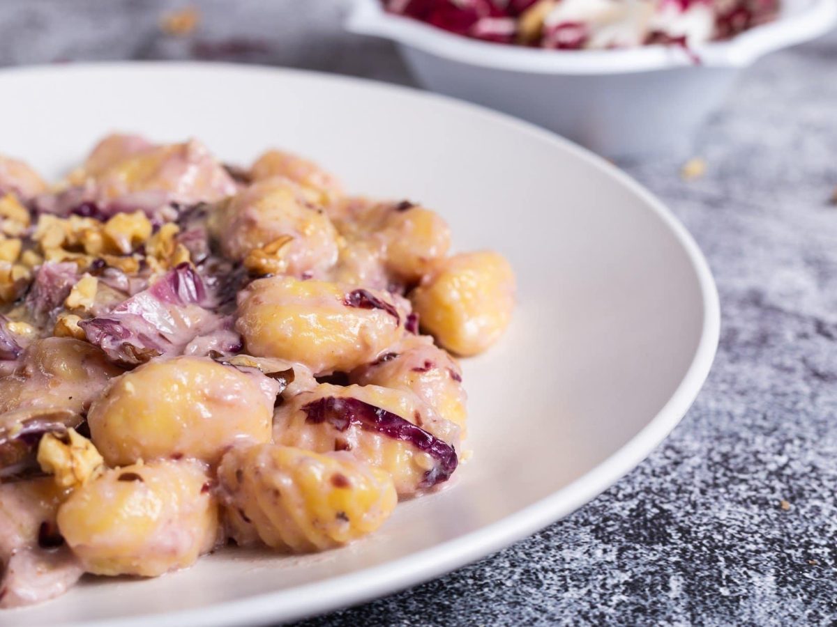 Draufsicht schräg: Ein Teller Gnocchi mit Radicchio in einer Walnuss-Sauce auf grauem Untergrund.