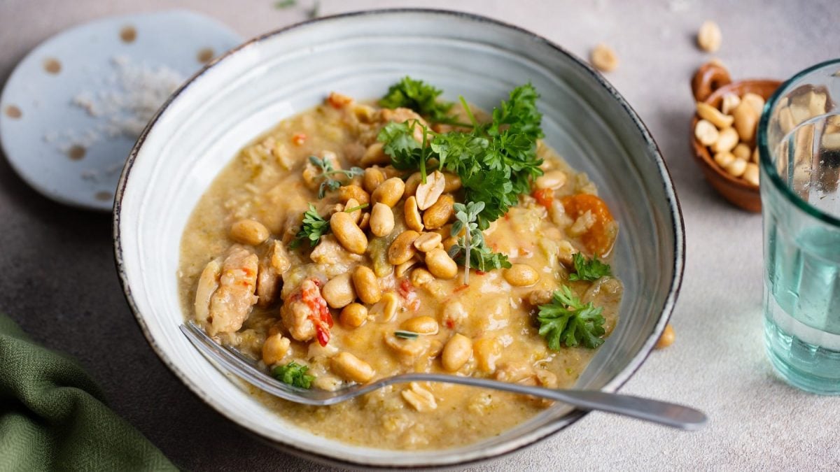 Eine graue Schale mit der Erdnuss-Bohnen-Suppe auf grauem Untergrund. Alles von schräg oben fotografiert.