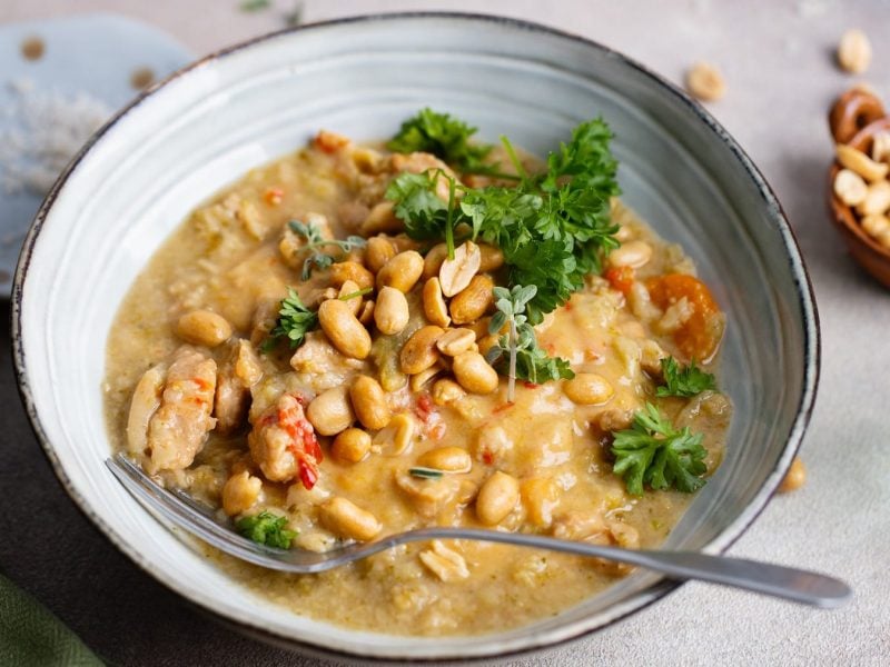 Eine graue Schale mit der Erdnuss-Bohnen-Suppe auf grauem Untergrund. Alles von schräg oben fotografiert.