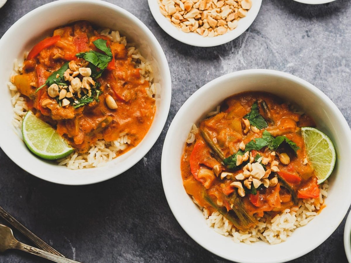 Zwei Schalen mit Erdnuss-Curry, garniert mit gehackten Erdnüssen und einer Limettenscheibe. Das Ganze ist angerichtet auf einem Tisch mit grauer, melierter Platte.