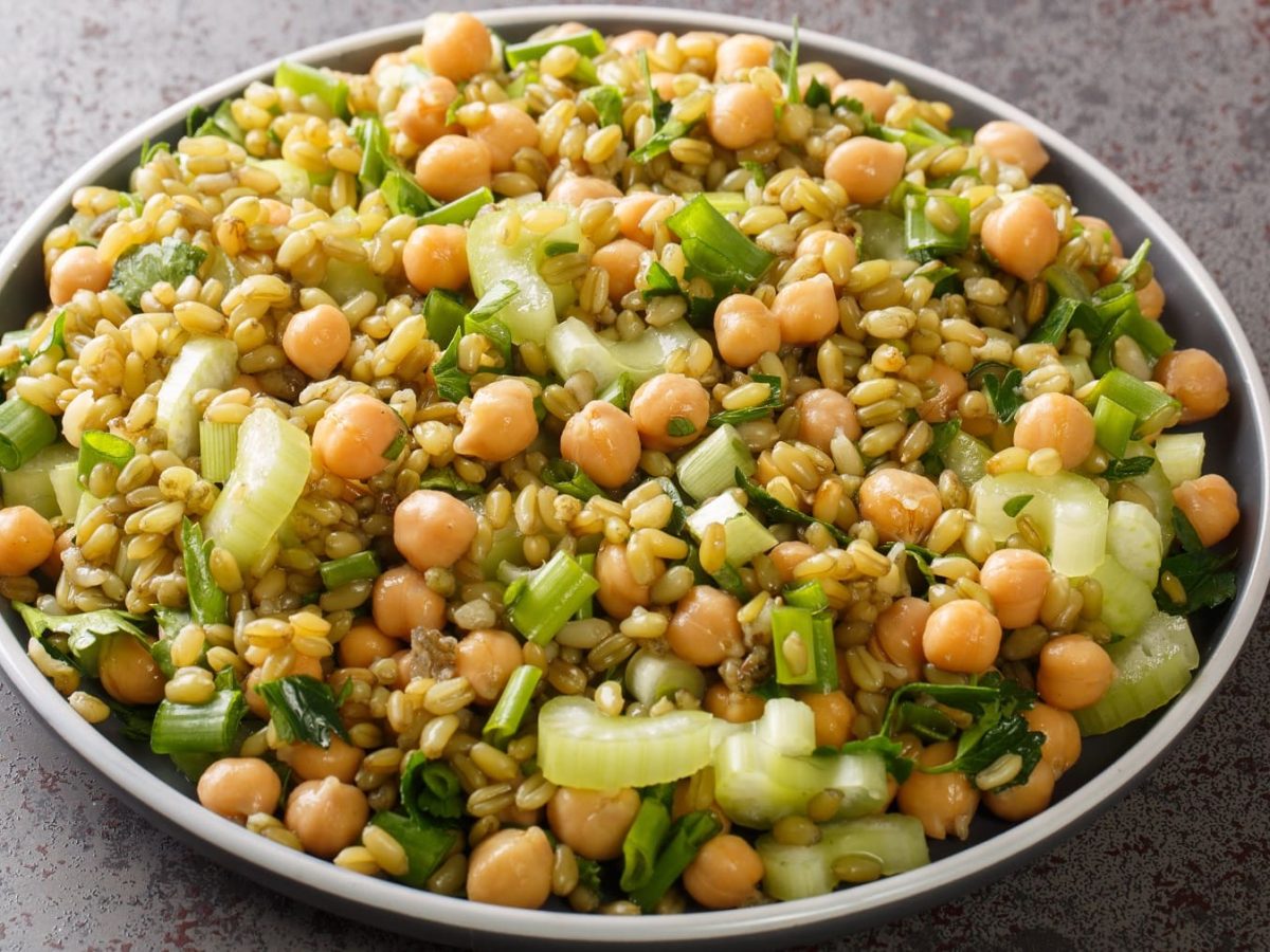 Ein grauer Teller mit dem Freekeh-Salat auf grauem Untergrund. Alles von schräg oben fotografiert.