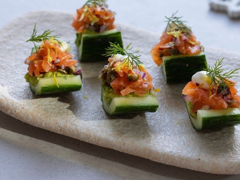 5 kleine Fingerfood-Snacks mit Avocado und Räucherlachs auf einem weißen Teller von schräg oben fotografiert.