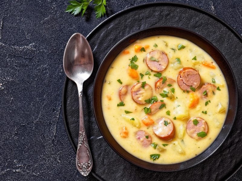 Eine schwarze Schüssel mit der Kartoffelsuppe auf dunklem Untergrund. Alles direkt von oben fotografiert.