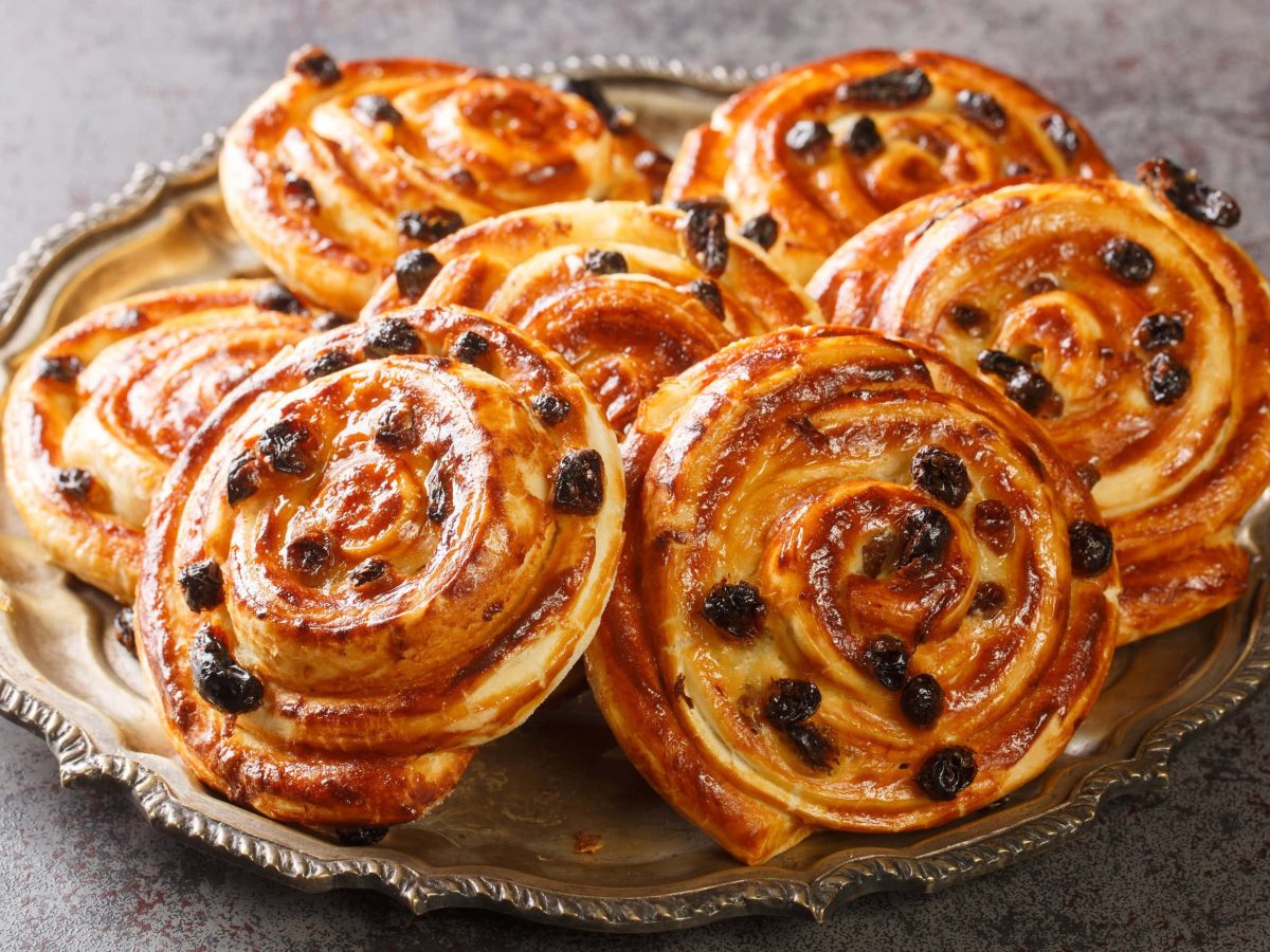 Mehrere Puddingschnecken auf einem silbernen Teller und grauen Untergrund. Alles von der Seite fotografiert.