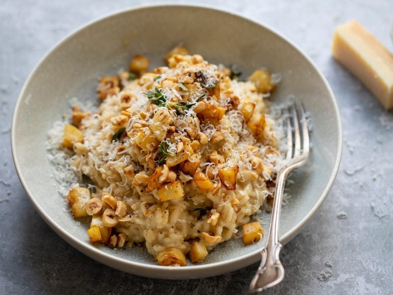 Eine graue Schale mit dem Sellerie-Risotto auf grauem Untergrund von schräg oben fotografiert.