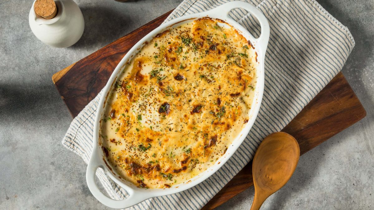 Scalloped Potatoes – cremiges, käsiges Kartoffelgratin in weißer Auflaufform. Draufsicht.