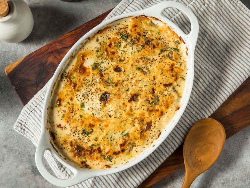 Scalloped Potatoes – cremiges, käsiges Kartoffelgratin in weißer Auflaufform. Draufsicht.