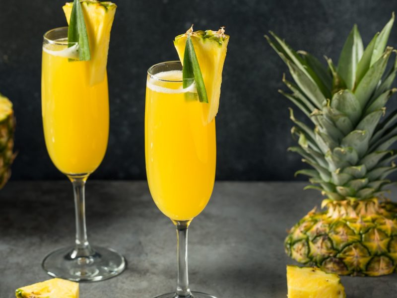 Zwei Gläser Ananas-Mimosa neben frischer Ananas.