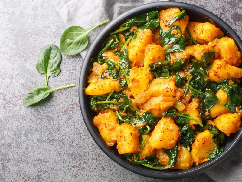 Ein schwarzer Topf mit Saag Aloo auf einem grauen Tisch.