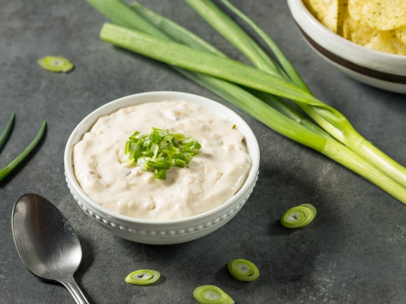 Ein weißes Schälchen mit dem Sour Cream-Dip auf grauem Untergrund.