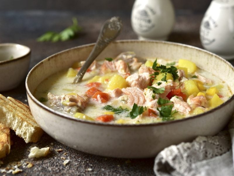 Draufsicht schräg: Eine Teller amerikanische Chowder mit Lachs steht auf einem Holztisch. Dahinter stehen ein Salz- und ein Pfefferstreuer.