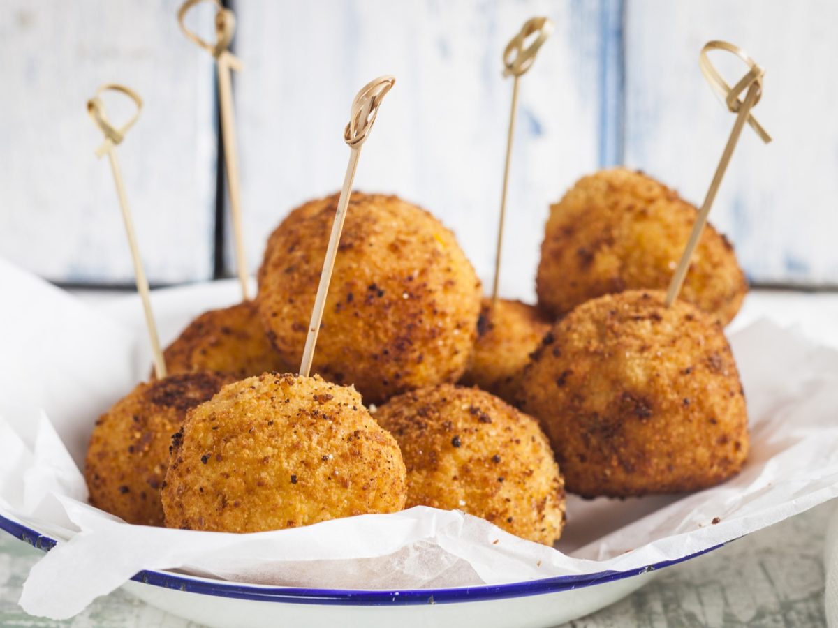 Bitterballen auf einem weißen Teller mit blauem Rand von der Seite fotografiert.