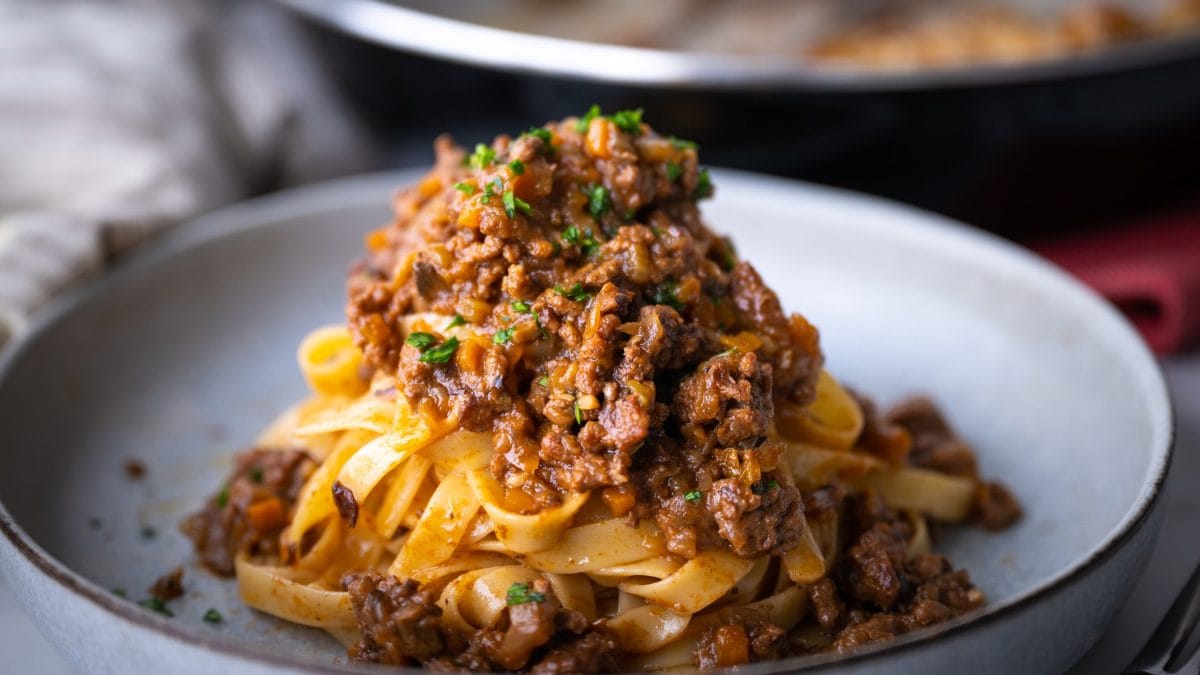 Ein weißer Teller mit Pasta und Bolognese von der Seite und nah fotografiert.