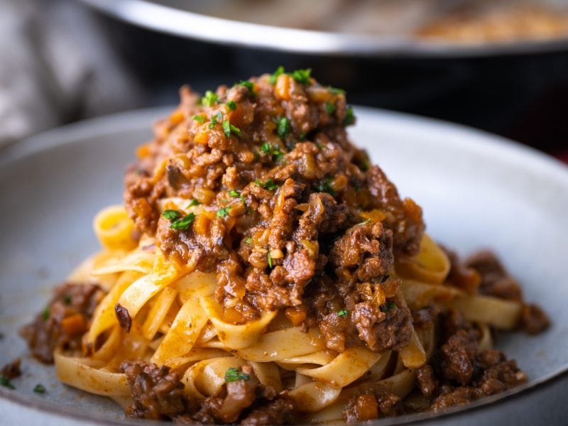 Ein weißer Teller mit Pasta und Bolognese von der Seite und nah fotografiert.