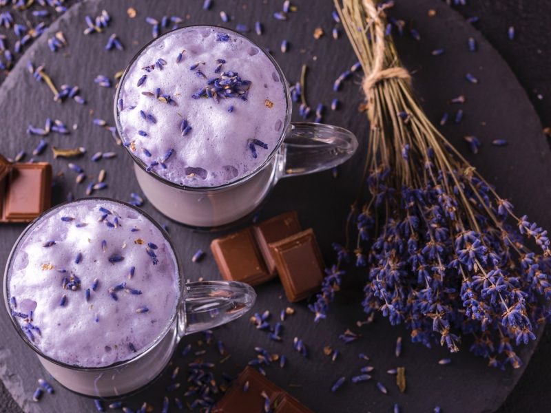 Cappuccino mit Lavendel und Schokolade in zwei Gläsern. daneben Schokoladenstücke und ein Lavendelbund.