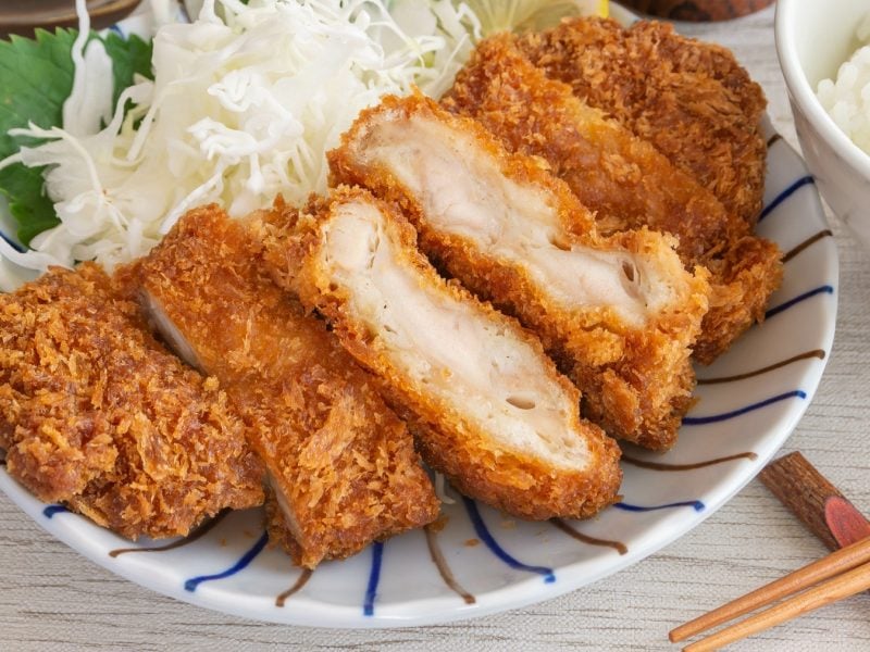 Geschnittenes Chicken Katsu mit Sprossen und Reis auf einem Teller.