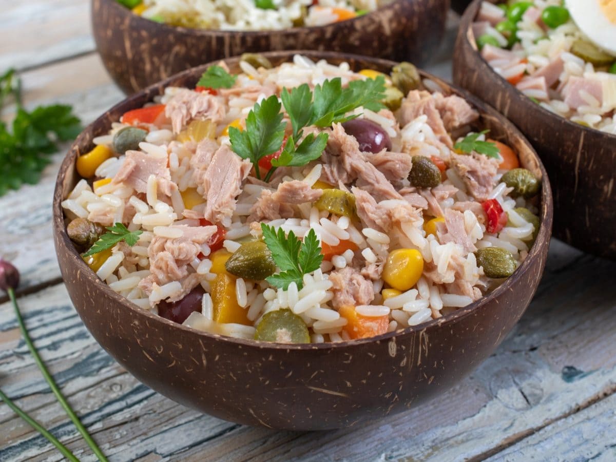 Draufsicht, schräg: Zwei Schalen Italienischer Reissalat mit Thunfisch. Die stehen auf einer Holzplatte. Drum herum liegt frische Petersilie.