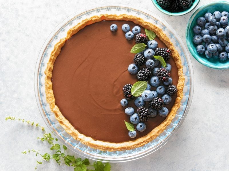 Draufblick: eine runde Schoko-Mousse-Tarte mit Beeren in einer Form. Daneben steht eine runde Schale mit Beeren.