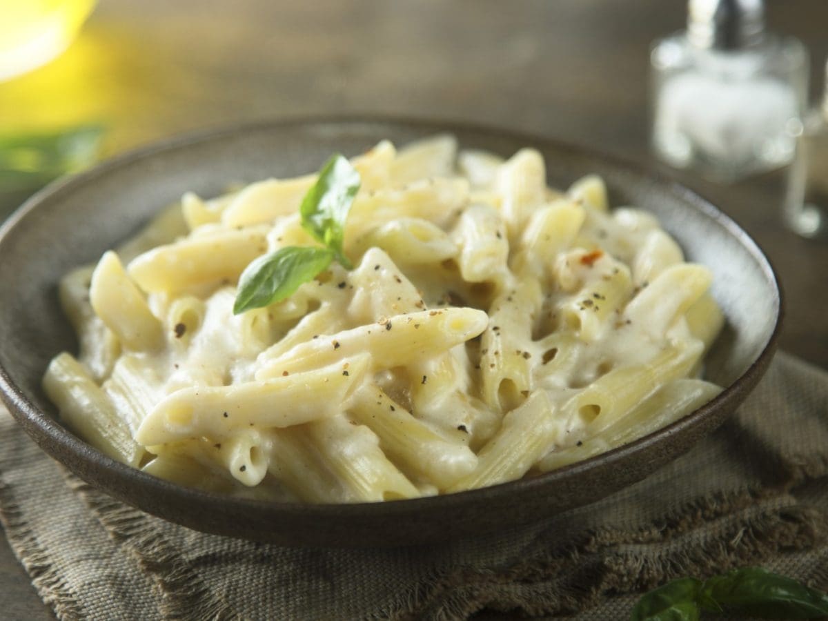 Ein dunkelbrauner Teller mit der Pasta auf einem dunklen Holztisch. Alles von schräg oben fotografiert.