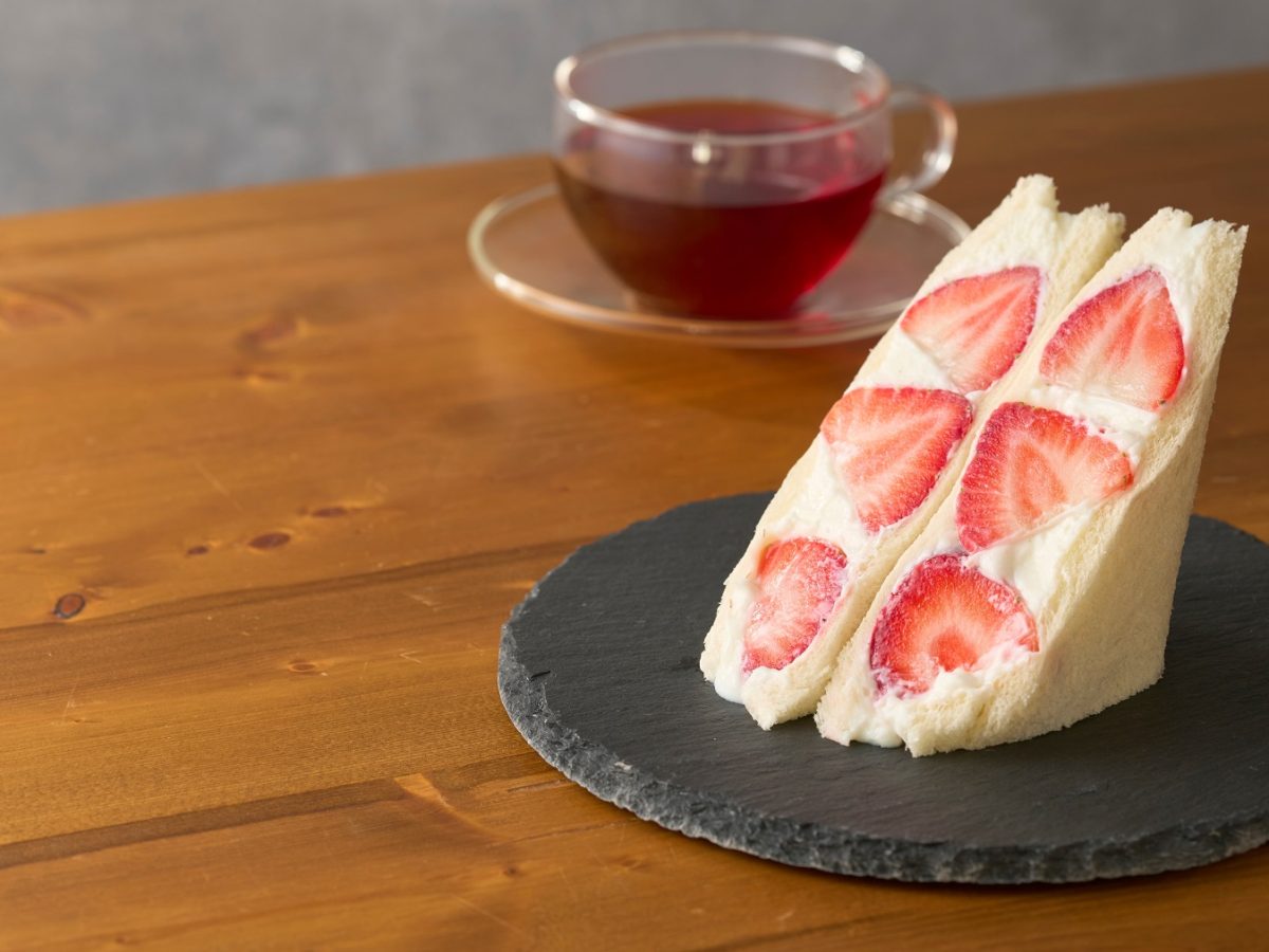 Aufgeschnittenes Fruit Sando mit Erdbeeren. Daneben eine Tasse Tee.