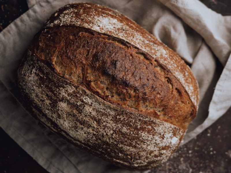 Glutenfreies Sauerteigbrot auf einem hellgrauen Geschirrtuch auf schwarzem Hintergrund.