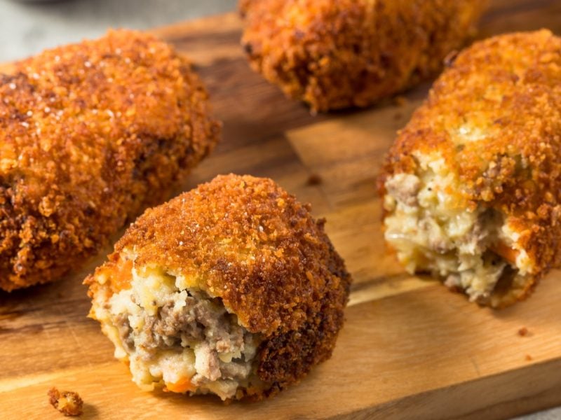 Einige Hackfleisch-Kroketten sehr nah fotografiert auf einem Holzbrett serviert.