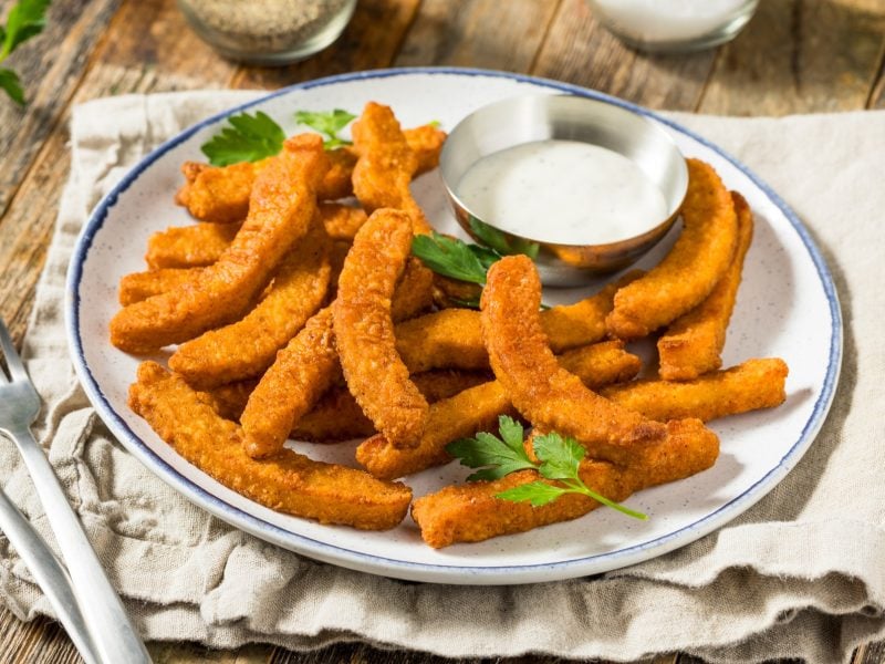 Mehrere Halloumi-Fries auf einem weißen Teller mit blauem Rand. Alles auf einem rustikalen Holztisch fotografiert.