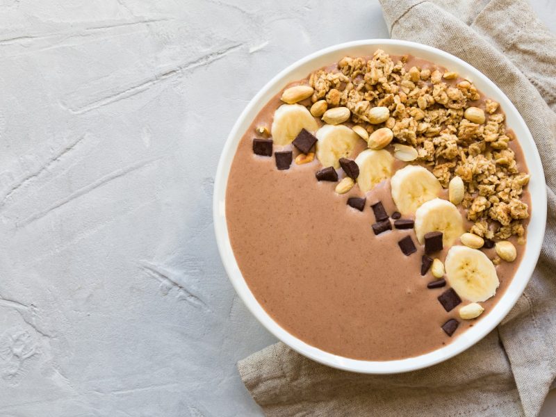 Kaffee-Smoothie-Bowl in einer weißen Schüssel auf einem weißen Hintergrund. Rechts ein beiges Geschirrtuch.