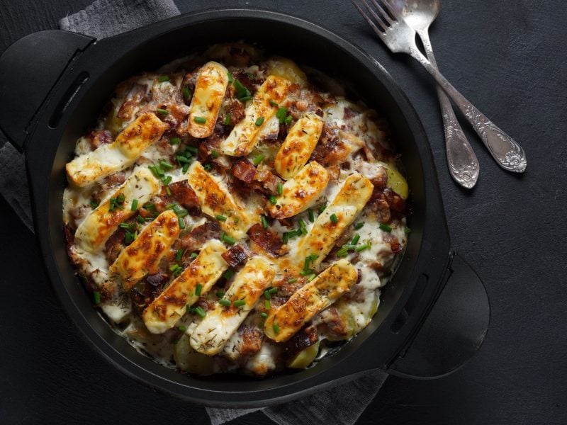 Eine schwarze Auflaufform mit dem Kartoffel-Rosenkohl-Gratin auf einem dunklen Untergrund.