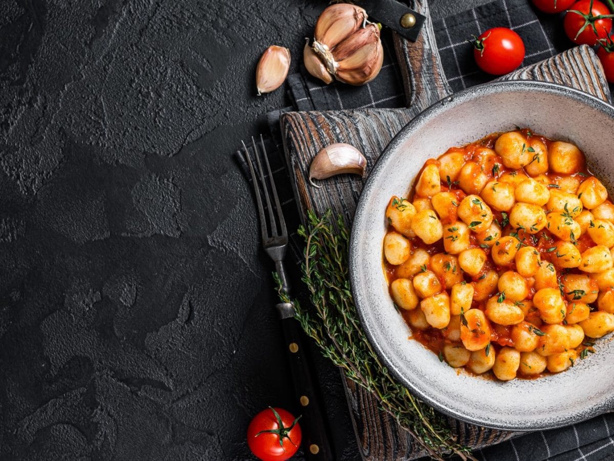 Draufsicht: Knoblauch-Gnocchi mit Tomatensauce auf schwarzem Untergrund.