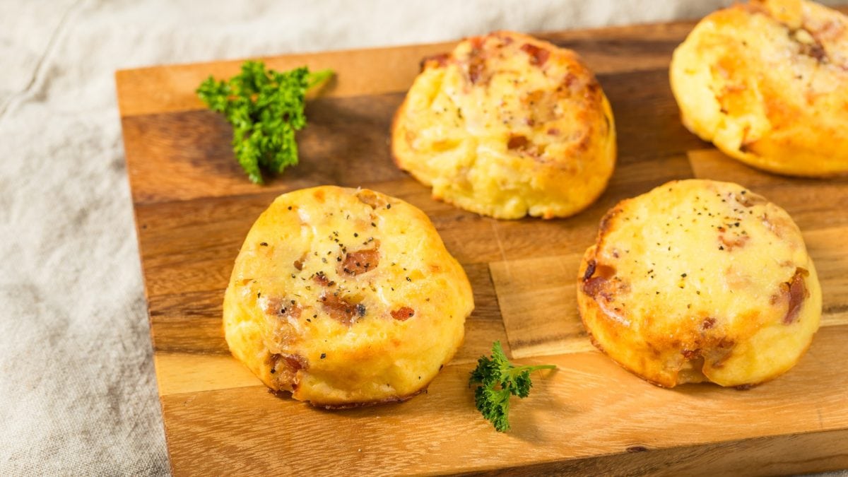 Ein Holzbrett mit vier kleinen Kartoffel-Soufflés auf hellem Untergrund. Alles von schräg oben fotografiert.