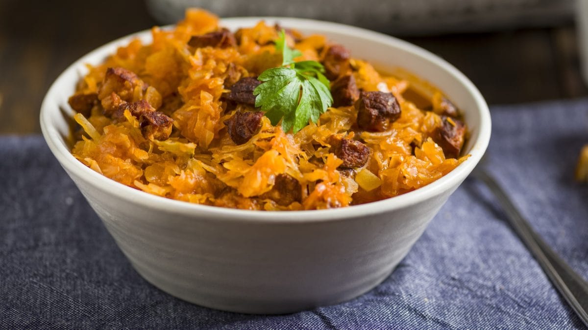 Eine hellgraue Schale mit dem Paprika-Kohl auf einem Holztisch mit dunkelblauem Stoff. Alles schräg von der Seite fotografiert.