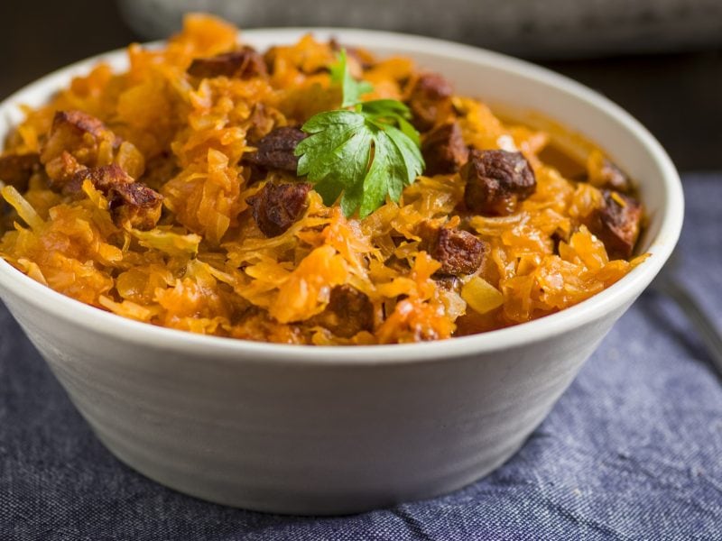 Eine hellgraue Schale mit dem Paprika-Kohl auf einem Holztisch mit dunkelblauem Stoff. Alles schräg von der Seite fotografiert.