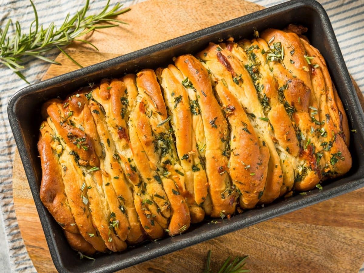 Eine Kastenform mit dem Pull-Apart-Bread auf einem Holzschneidebrett und grauem Tisch.