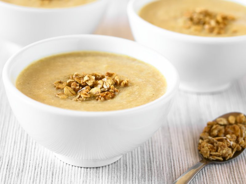 Rhabarber-Mousse in weißen Schüssel mit Granola-Topping. Daneben ein goldener Löffel mit Granola.