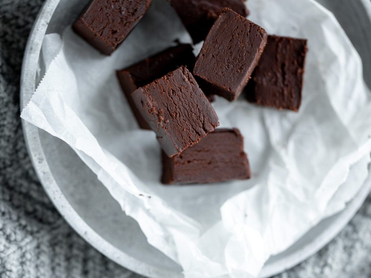 Rohkost-Brownies auf weißem Backpapier auf einem weißen Teller. Der Hintergrund ist grau.