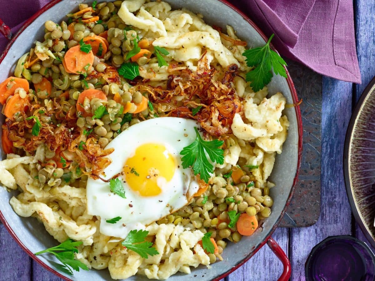 Draufsicht: Spätzle-Linsenpfanne mit Spiegeleiern in einer Pfanne auf blauem Holzuntergrund.